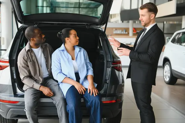 Araba satıcısı, modern bayilikte Afro-Amerikan bir çifte araç bagajı sunuyor.