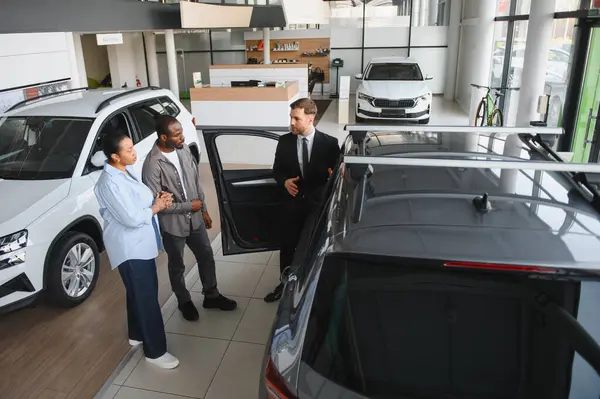 Araba satıcısı Afrikalı Amerikalı bir çifte yeni bir arabanın özelliklerini sunuyor. Mükemmel araçlarını seçmelerine yardımcı oluyor.