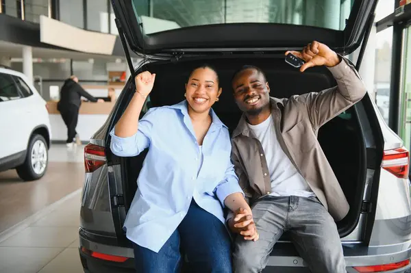 Yeni arabalarının bagajında el ele tutuşan ve araba anahtarlarını gösteren heyecanlı bir çift.