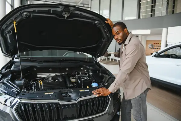 Otomobil galerisinde yeni bir aracın motorunu inceleyen adam, bilgilendirilmiş bir satın alma kararı için seçenekleri dikkatlice değerlendiriyor.