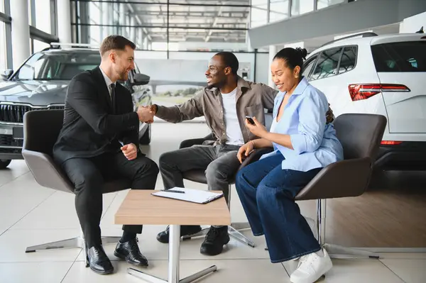 Yeni arabalarını satın aldıktan sonra bir galeride bir araba satıcısıyla tokalaşan çift.