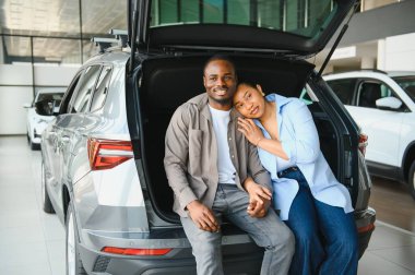 Afrika kökenli Amerikalı çift el ele tutuşup yeni arabalarının bagajında oturuyorlar. Araba galerisinin keyfini çıkarıyorlar.