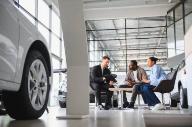 Araba satıcısı, araba galerisindeki koltuklarda oturan Afrikalı Amerikalı çifte satış sözleşmesini açıklıyor.