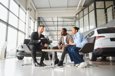 Araba satıcısı, modern bir galeride yeni bir araba alan bir çifte yeni bir sözleşme sunuyor. Seçenekleri ve detayları tartışıyor.