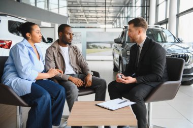 Araba satıcısı, Afrikalı Amerikalı bir çifte yeni bir araba teklifi sunuyor. Finansal seçenekleri tartışıyor ve modern bir galeri galerisinde anlaşmalar satın alıyor.