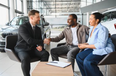 Modern bir galeride yeni bir araba için anlaşma yaptıktan sonra bir araba satıcısıyla tokalaşan mutlu çift.