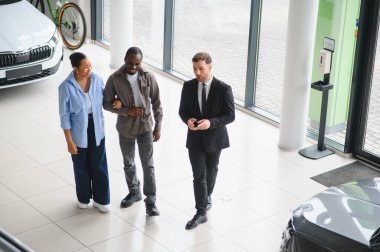 Araba satıcısı Afrika kökenli Amerikalı bir çifte yeni arabalarını modern bir bayiden seçmelerine yardım ediyor.