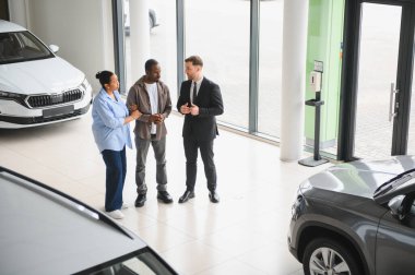 Araba satıcısı, modern otomobil bayiliğinde Afro-Amerikan çifte araç sunuyor. Tavsiye veriyor ve satın alma seçeneklerini tartışıyor.