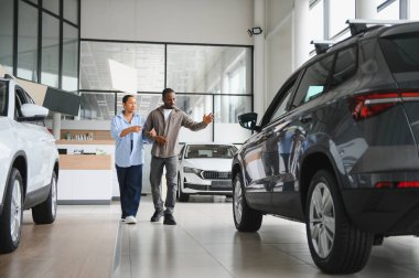 Afro-Amerikalı çift galeride yeni bir SUV araba seçiyor, satış müdürüyle tartışıyorlar.