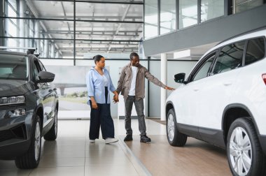 Afrika kökenli Amerikalı çift el ele tutuşuyor, seçenekleri değerlendiriyor ve bir galeride yeni bir araba seçerken tercihlerini tartışıyorlar.