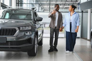 Afro-Amerikalı çift el ele tutuşup galeride yeni bir SUV seçiyorlar. Satın alma yolculuğunun heyecanıyla eğleniyorlar.