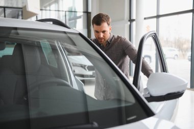 Galeride yeni bir beyaz arabayı teftiş eden adam kapıyı açıyor ve test sürüşüne hazırlanıyor.