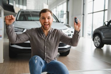 Yeni bir aracın satın alınmasını kutlayan mutlu bir adam, heyecan dolu bir galerinin anahtarlarını gururla tutuyor.