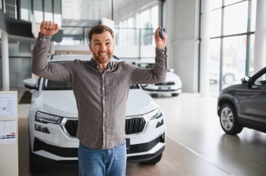 Mutlu adam yeni bir araba almayı kutluyor. Anahtarları elinde tutuyor ve galeride silah kaldırıyor.