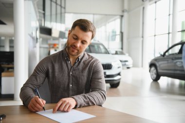 Modern bir galeride yeni bir araba alımı sözleşmesi imzalayan memnun müşteri, anlaşmayı sonuçlandırıyor.