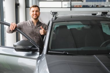 Şık bir galeride araba seçeneklerini araştıran hevesli bir adam yeni bir araç seçmek için heyecan ve ilgi gösteriyor.