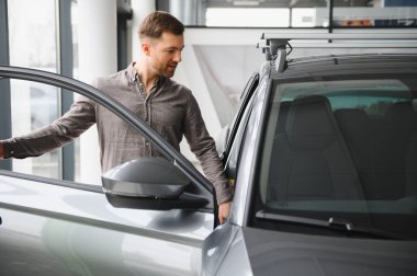 Yakışıklı bir adam araba galerisinde yeni bir araba seçiyor, kapıyı açıyor ve modern bir sedan 'ın içini inceliyor.