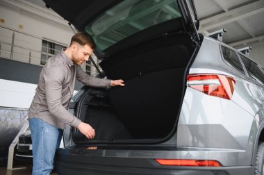 Pratik ve depolama kapasitesini göz önüne alarak modern bir cipin kargo bölümünü otomobil galerisinde inceleyen bir adam.