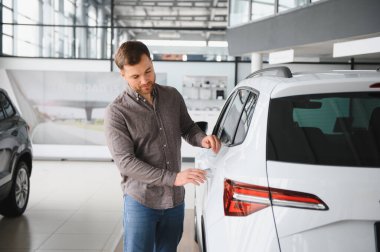 Müşteri galeride yeni bir beyaz arabayı kontrol ediyor, araba gövdesine dokunuyor ve detaylarına bakıyor.