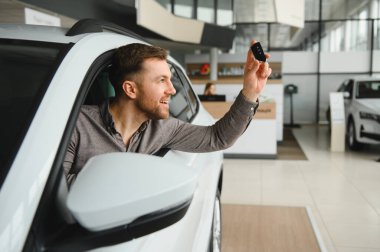 Gülümseyen müşteri yeni araba anahtarını gururla tutarken aynı zamanda yeni arabasının rahatlığının keyfini çıkarıyor.