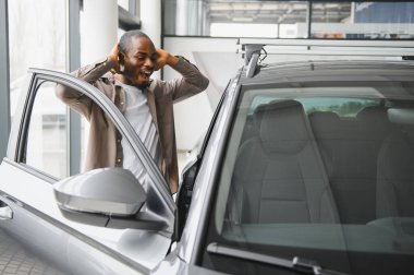 Bir galeride heyecanlı bir adam. Elleriyle kafasına dokunurken inanamadığını ifade ediyor. Yeni bir araba almanın mutluluğunu kutluyor.