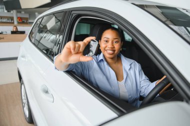 Gülümseyen kadın yeni bir arabada otururken arabanın anahtarlarını gösteriyor. Otomobil galerisinden aldığı için mutlu.
