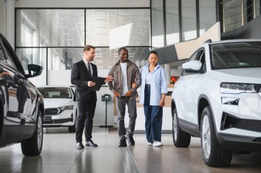 Araba satıcısı, modern bir galeride Afro-Amerikan bir çifte yeni bir araba sunuyor. Hayallerindeki aracı seçmek için yardım ve rehberlik öneriyorlar.