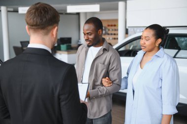 Satıcının elinde sözleşmesi var. Afro-Amerikan çiftlere otomobil galerisinden yeni araba almalarını açıklıyor.