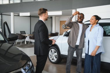 Heyecanlı çift yeni araba anahtarlarını bir araba galerisinde satıcıyla alışverişlerini kutluyorlar.