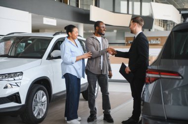 Mutlu Afro-Amerikan çifti bir satıcıyla el sıkışıyor, yeni bir araba almak için bir galeriye gidiyorlar.