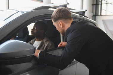 Araba satıcısı, bir galeride potansiyel bir Afro-Amerikan müşteriye yeni bir arabanın özelliklerini gösteriyor.