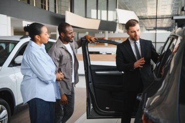 Araba satıcısı, bir galerideki birkaç müşteriye yeni bir arabanın özelliklerini sunuyor ve bilinçli bir karar vermelerine yardımcı oluyor.