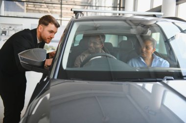 Modern bir galeride araba almak isteyen Afro-Amerikan bir çifte yeni bir arabanın özelliklerini gösteren profesyonel bir araba satıcısı.
