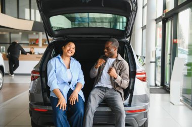 Galerideki yeni arabalarının açık bagajında oturan heyecanlı çift, arabanın özelliklerini tartışıyor ve anın tadını çıkarıyor.