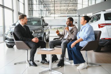 Afrika kökenli Amerikalı bir çift, bir satış elemanı ile pazarlık ederken aynı zamanda yeni ideal arabalarını bir galeride seçiyorlar.