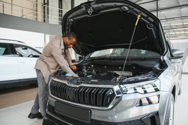 Bir araba galerisinde yeni bir cipin motorunu inceleyen bir adam satın alma kararını dikkatlice değerlendiriyor ve seçenekleri değerlendiriyor.