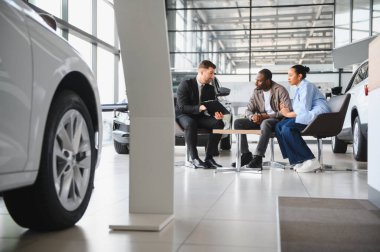 Araba satıcısı, bir galeride Afro-Amerikan çifte sözleşmenin detaylarını gösteriyor ve yeni bir aracın alımını tartışıyor.