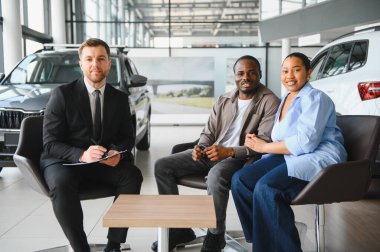 Araba satıcısı genç bir çiftle otururken not alıyor. Yeni arabalarını galeriden seçiyorlar.