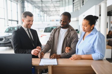 Mutlu satıcı, Afrikalı Amerikalı çifte yardım ediyor. Modern bir galeride yeni bir araba alımı için kontrat imzalıyor.