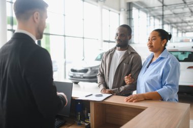 Afroamerikan çift yeni bir araba seçiyor, araba satıcılarının karakteristik ve fiyatlarla ilgili açıklamalarını dinliyorlar.