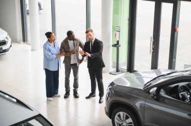 Araba satıcısı, Afrika kökenli Amerikalı çifte yeni aracın özelliklerini sunuyor. Modern araba galerisinde satın alma kararı veriyor.