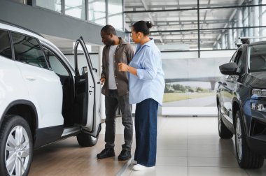 Afrika kökenli Amerikalı çift araba galerisindeki yeni beyaz SUV 'u inceliyor, araç alma konusunda karar veriyorlar.