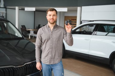 Mutlu müşteri galeride araba anahtarlarını gururla tutuyor. Yeni bir aracın satın alınmasını heyecan ve memnuniyetle kutluyorlar.