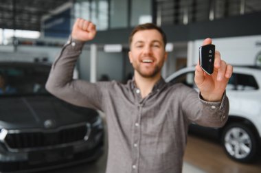 Galeride yeni araba alımını kutlarken arabanın anahtarını gösteren heyecanlı bir adam.