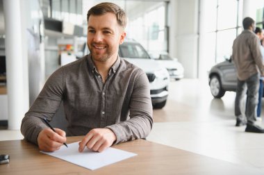 Mülkiyet ve yatırım heyecanını kutlamak için galeride yeni bir araba için sözleşme imzalayan mutlu bir müşteri.