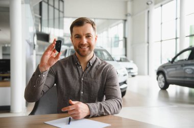 Etrafı araçlarla çevrili, parlak bir galeride gülümseyen bir adam arabanın anahtarını tutuyor. Yeni bir araba almaya karar veriyor, otomotiv seçimi sergiliyor.