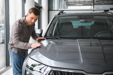 Adam galeride parlak gri bir cipi inceliyor, özellikleri dikkatlice değerlendiriyor ve satın alma kararını inceliyor.