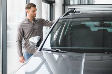 Parlak, çağdaş bir araba galerisinde aracı inceleyen bir adam satın alma kararı vermeden önce özelliklerini ve kalitesini değerlendiriyor.