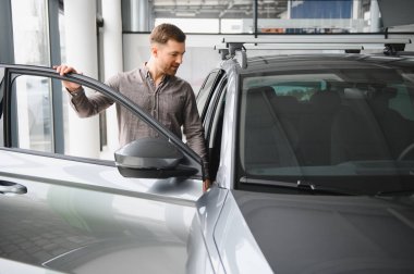 Parlak bir galeride şık ve modern bir arabayı inceleyen adam, bir sonraki araç alımının özelliklerini ve seçeneklerini göz önünde bulundurur.