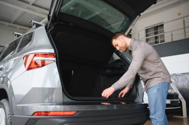 Bir araba galerisindeki yeni bir cipin bagajını inceleyen bir adam, kargo alanı ve pratik alanı göz önüne alındığında...